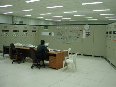 Control room with switchgear cabinets along two walls, an operator desk and a plant schematic.