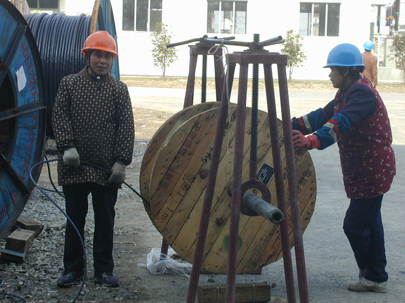 Two workers in hard hats pulling cable from a large wooden drum on the power plant construction site.